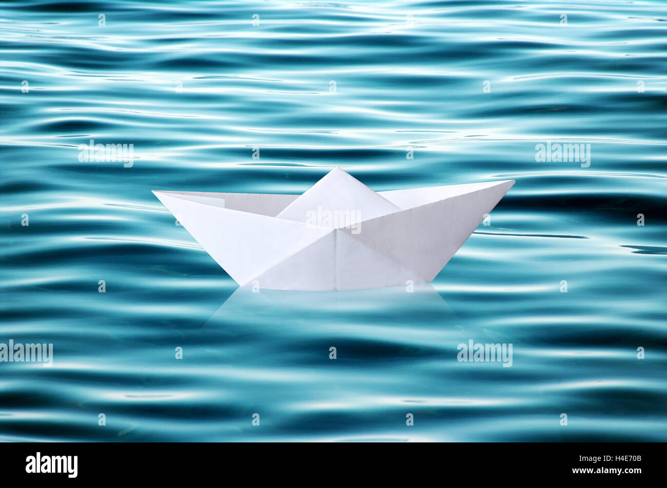 Small white folded paper origami boat floating on rippled blue water Stock Photo