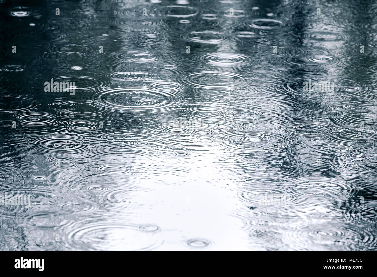 raindrops background with sky reflection and water circles on dark pavement Stock Photo