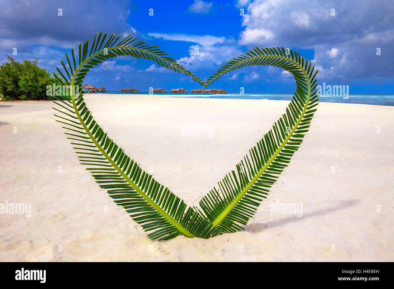 Heart made of palm tree leaves on tropical island with overwater bungalows in the background. Stock Photo