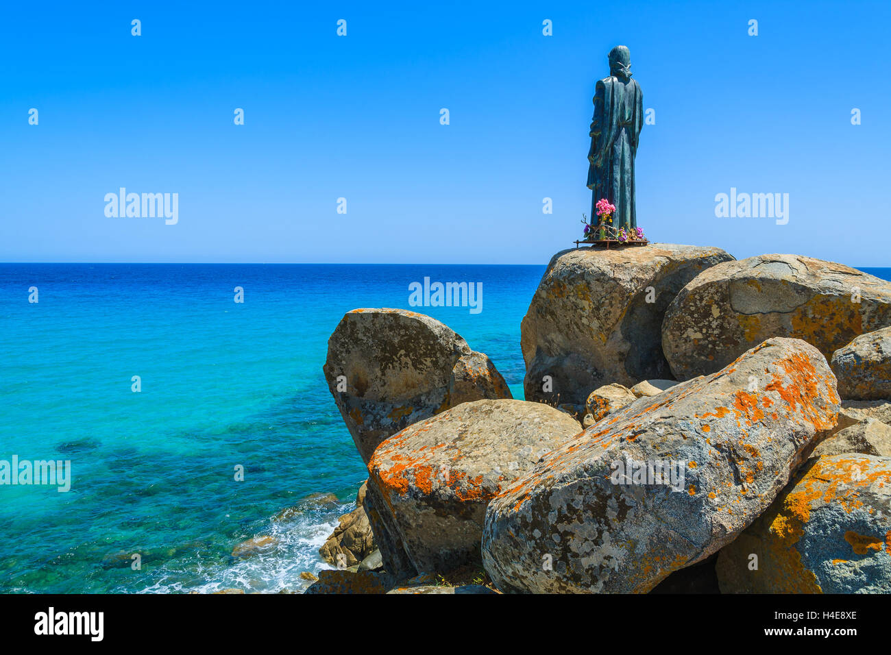 Jesus Christ sculpture on rocks at Cala Sinzias beach and sea view, Sardinia island, Italy Stock Photo