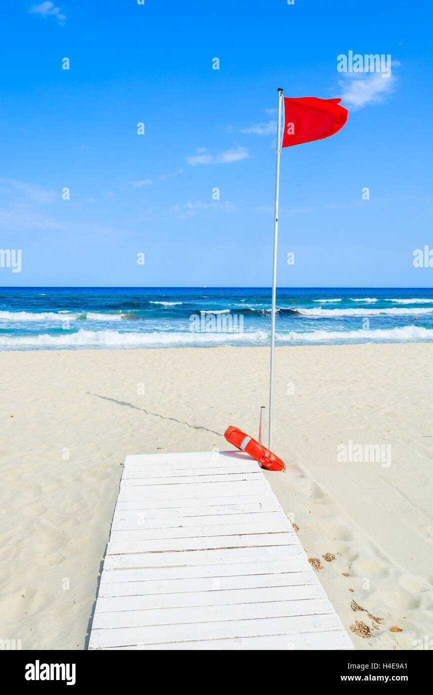 White wooden walkway on sandy beach with red flag on a pole, Porto Giunco bay, Sardinia island, Italy Stock Photo