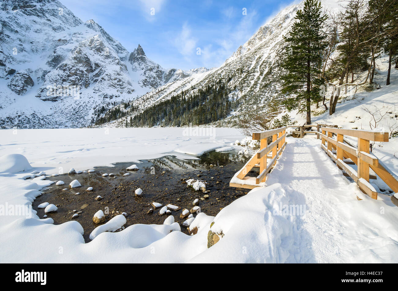 Wooden footbridge on hiking trail and covered with snow beautiful Morskie Oko lake in winter, High Tatra Mountains, Poland Stock Photo