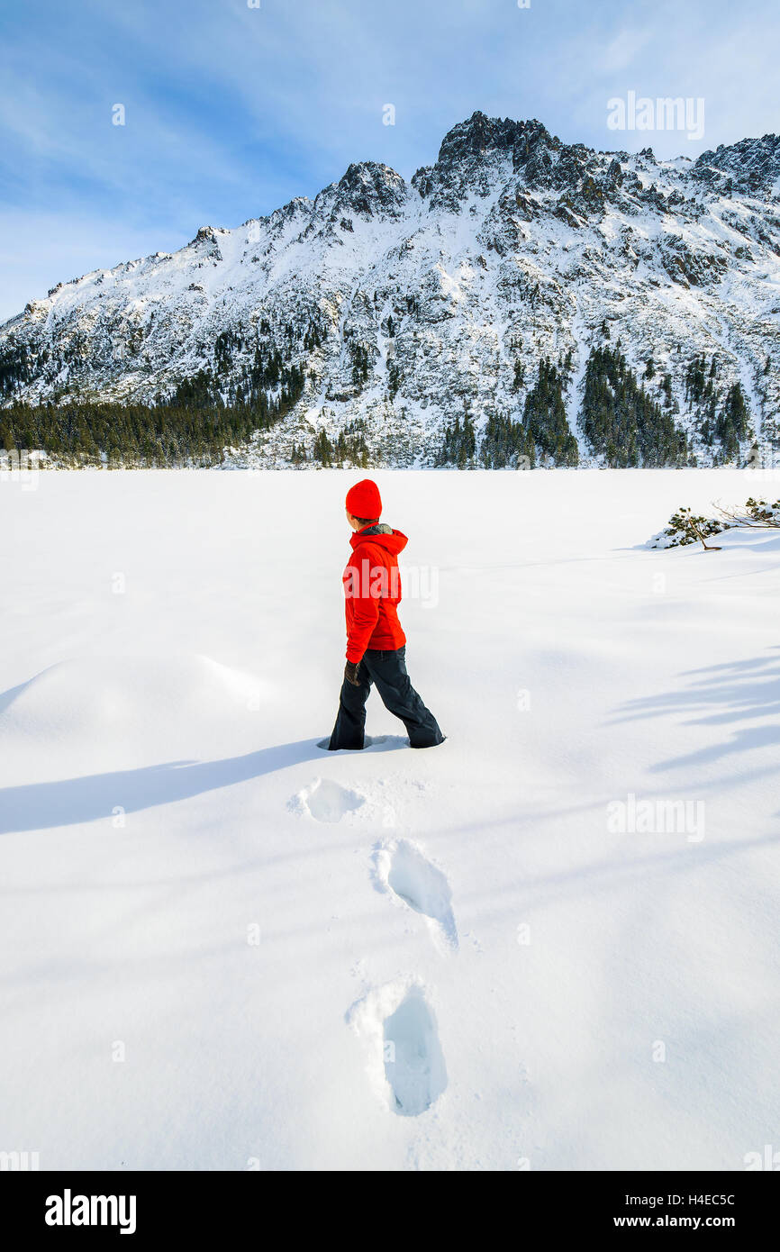 Young woman tourist in red jacket standing in deep fresh snow on frozen Morskie Oko lake in winter, Tatra Mountains, Poland Stock Photo
