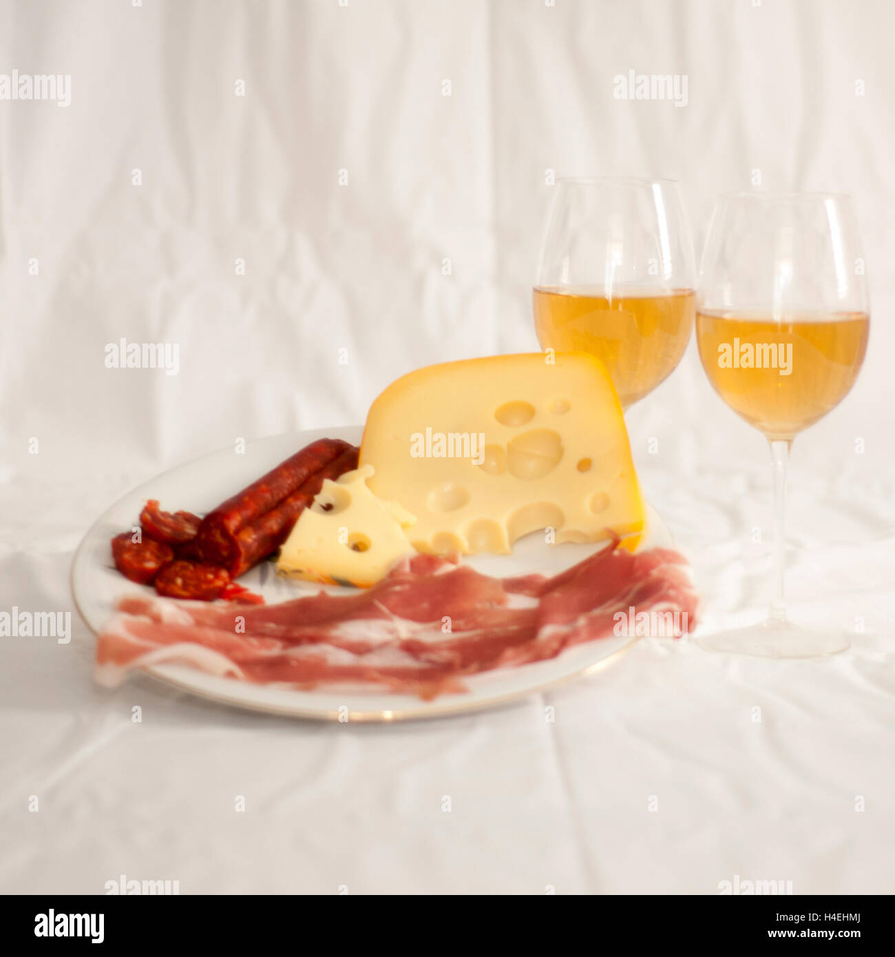 Plate of meats and cheese appetizer with two stemmed wine glasses with white wine on white cloth Stock Photo