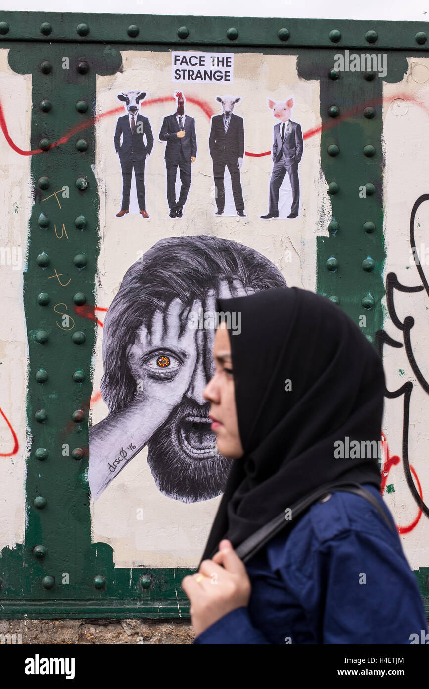 Muslim woman wearing a traditional black hijab or veil walking in front of a wall with mural in Brick lane Stock Photo