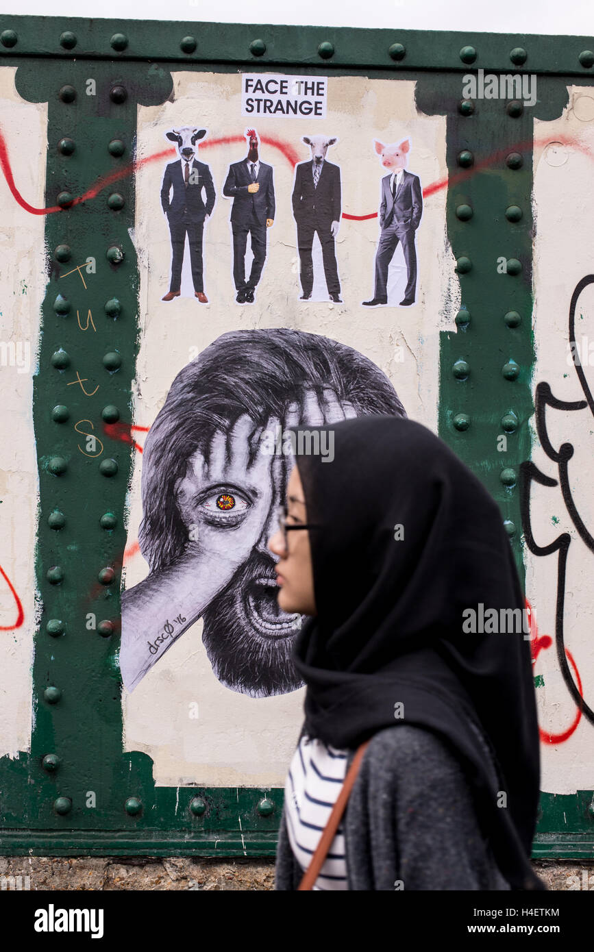 Muslim woman wearing a traditional black hijab or veil walking in front of a wall with mural in Brick lane Stock Photo