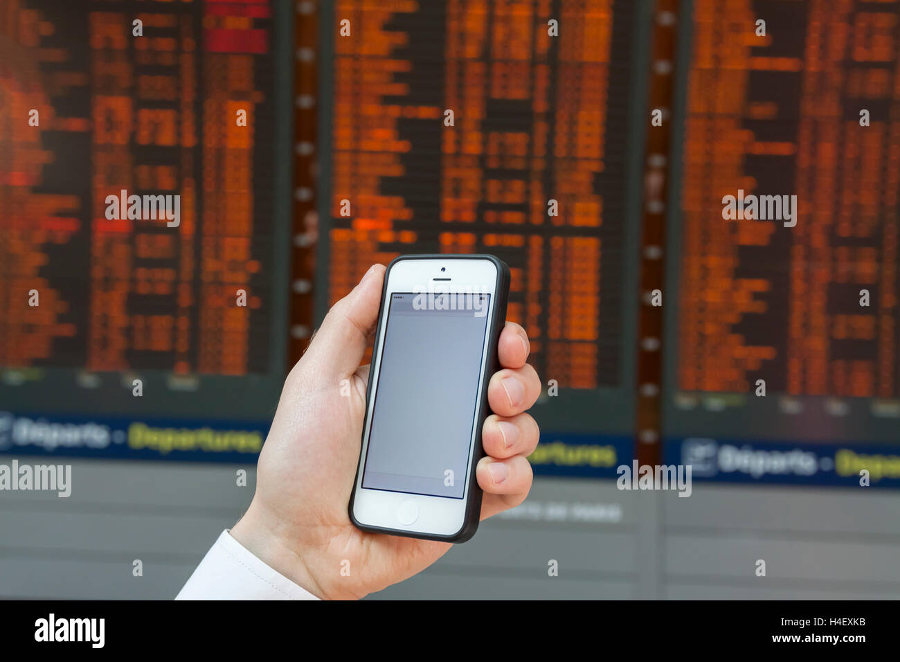 Checking smartphone screen at flight information board timetable in airport Stock Photo