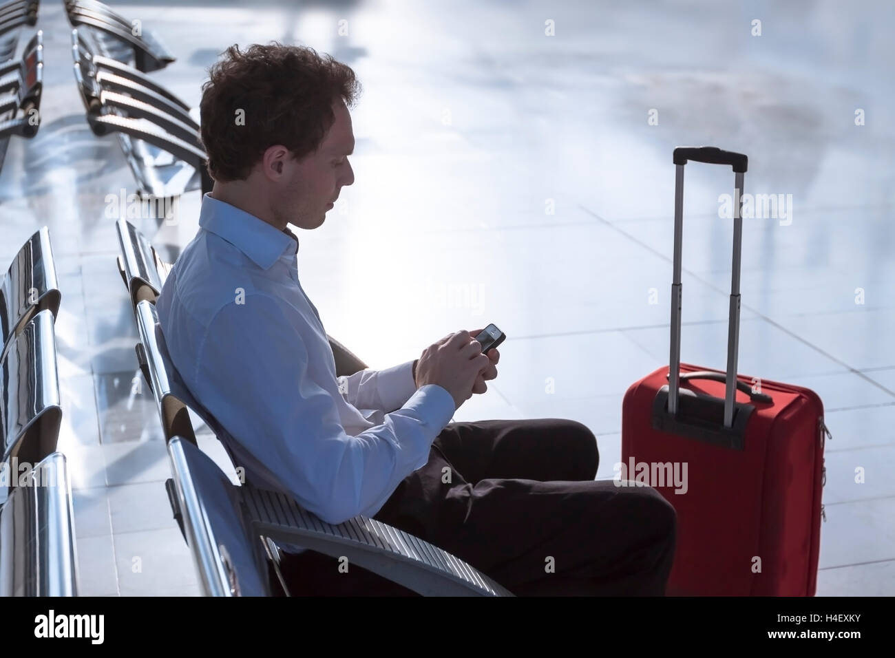 Businessman at airport with smartphone and suitcase checking emails before boarding Stock Photo