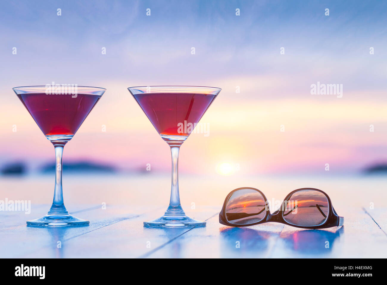 Two cocktails and sunglasses on a table of luxurious tropical beach resort restaurant with beautiful sunset in the background Stock Photo