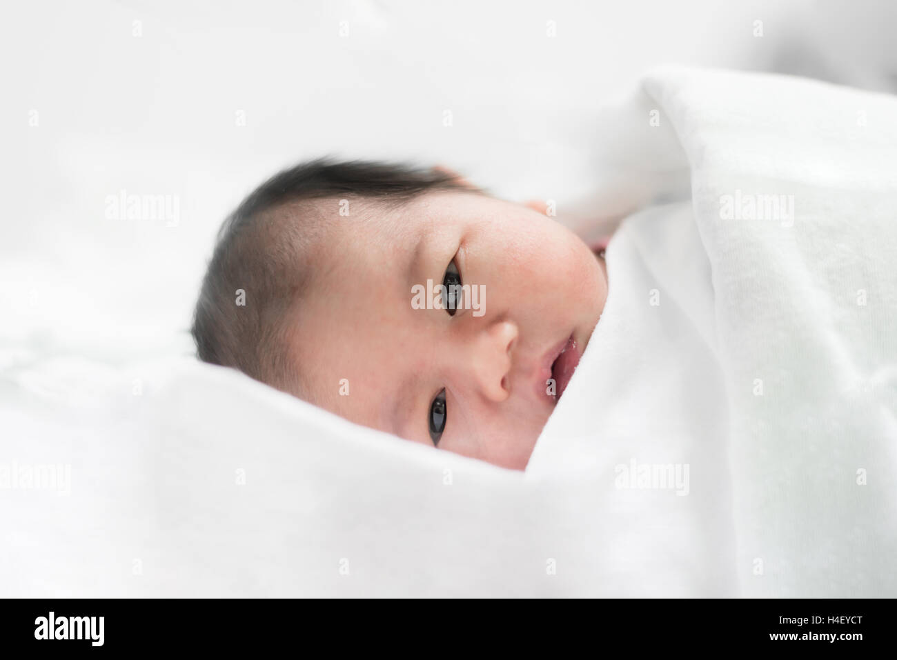 Asian newborn boy sleeping over his white bed covered with a blanket