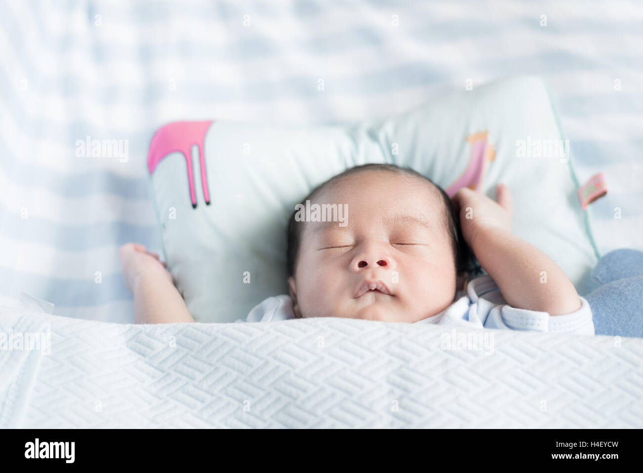 Asian newborn boy sleeping over his white bed covered with a blanket