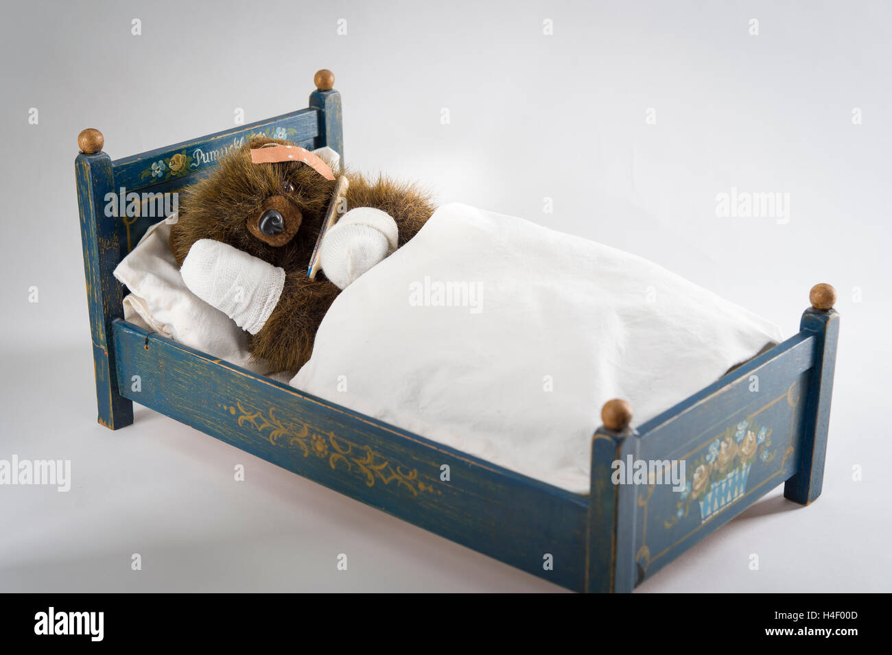 Sick Teddy Bear with head and paws bandaged, holding thermometer, in an original Pumuckl crib Stock Photo