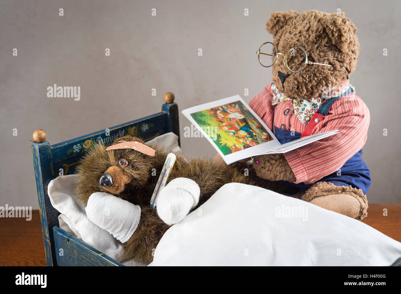 Sick Teddy Bear with bandaged paws and head, holding thermometer, in an original Pumuckl crib, Big Teddy Bear with glasses and Stock Photo