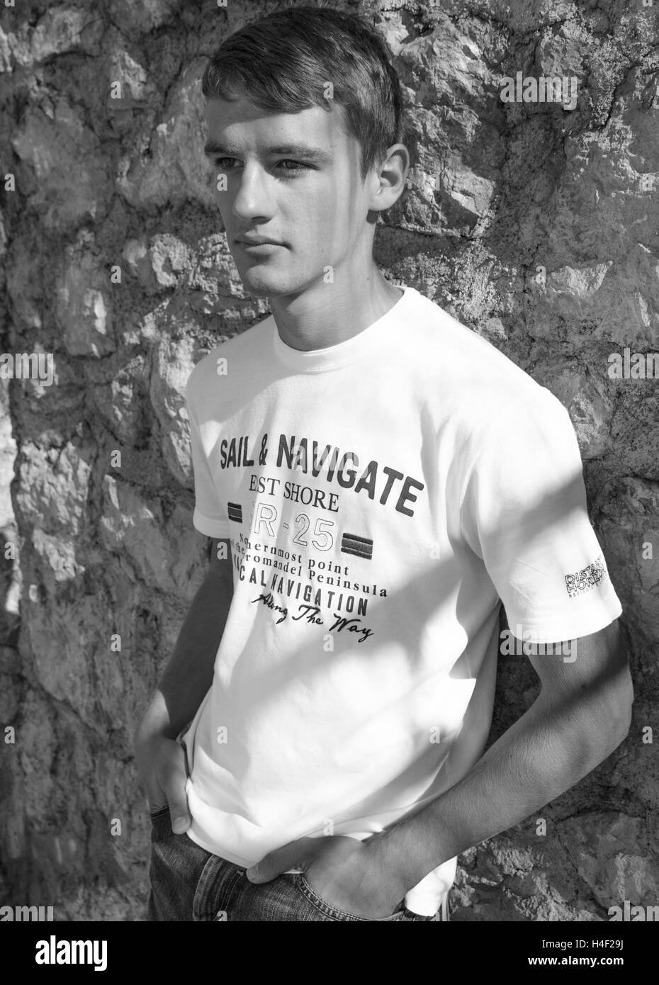 Black and white portrait of young handsome man leaning against stone wall Stock Photo