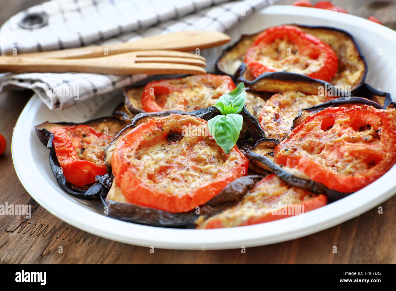 Delicious vegetarian pizza topping, roasted aubergine with tomatoes and basil on the plate on the wooden table Stock Photo