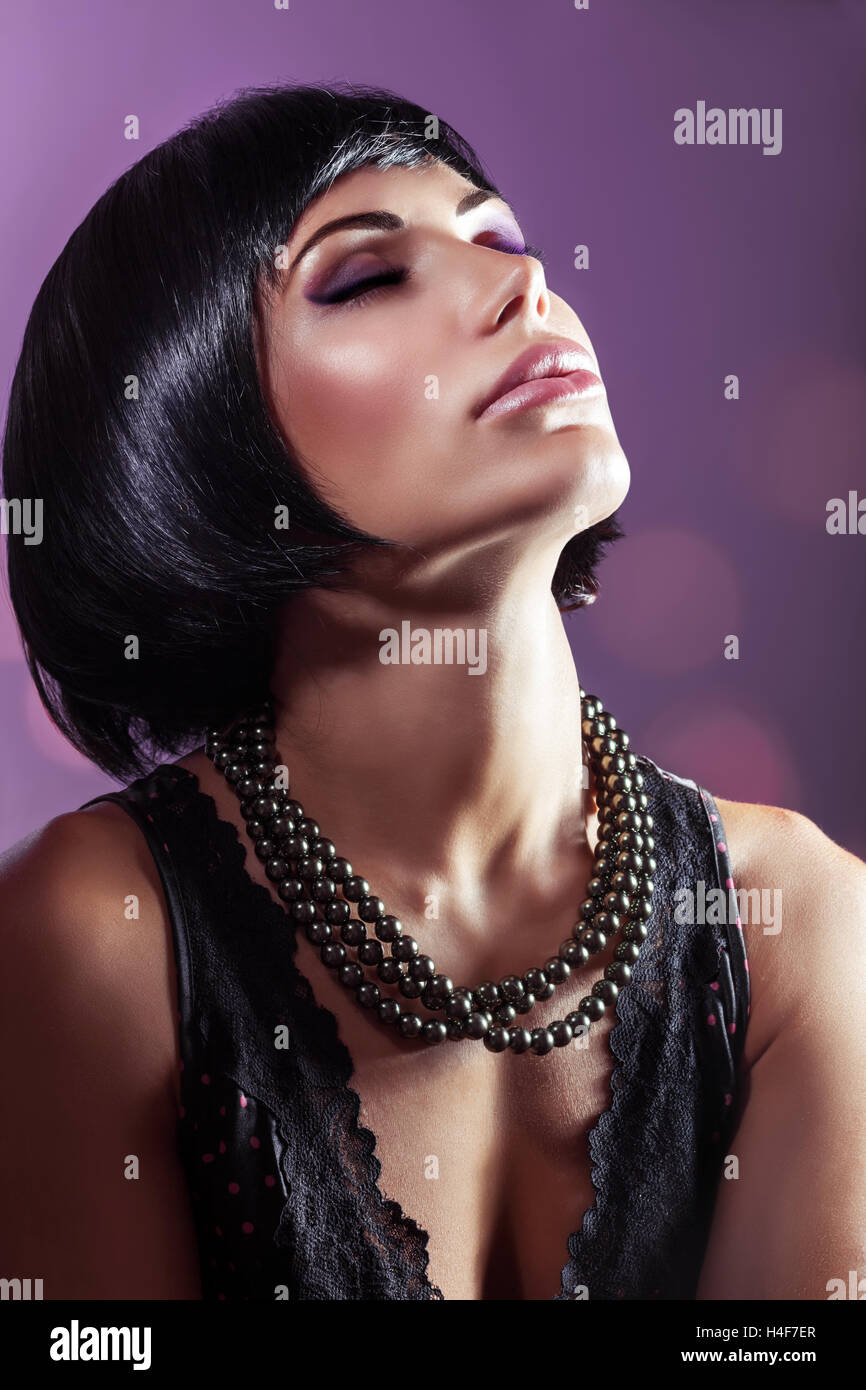 Sensual portrait of a beautiful woman with closed eyes over purple background, gorgeous lady with perfect hairstyle and makeup Stock Photo