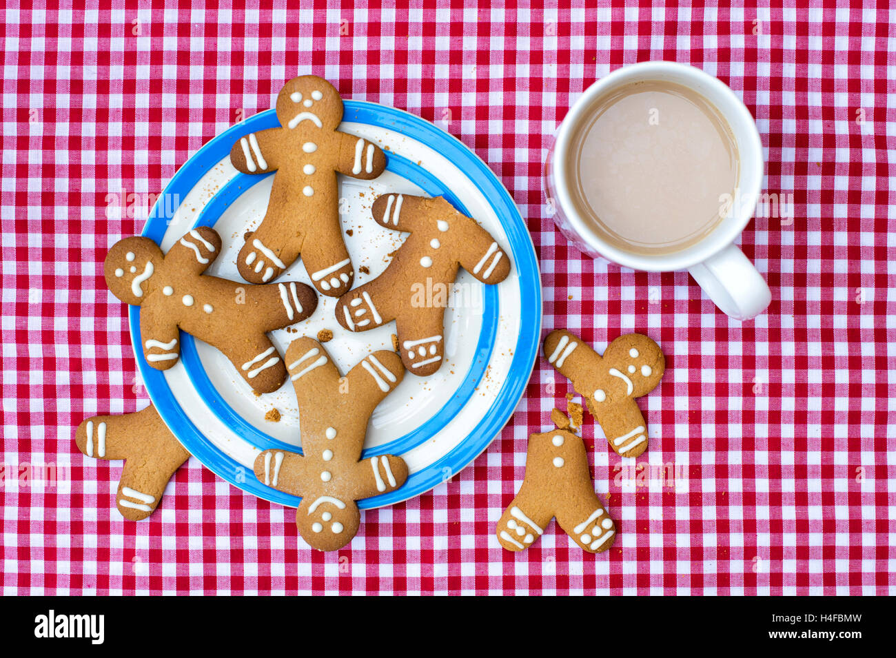 Gingerbread Men biscuits with happy sad and worried faces on a cornishware plate with a cup of tea Stock Photo