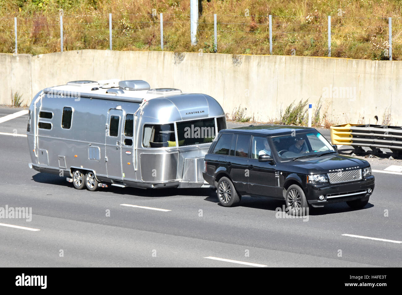 Driver and passenger in Range Rover car towing Airstream caravan driving along UK M25 motorway obscured numberplate Stock Photo