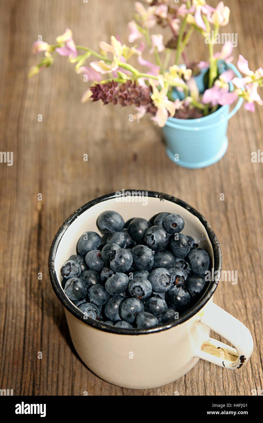 White enameled mug filled with billberries and wild orchid in small bucket on rustic table Stock Photo