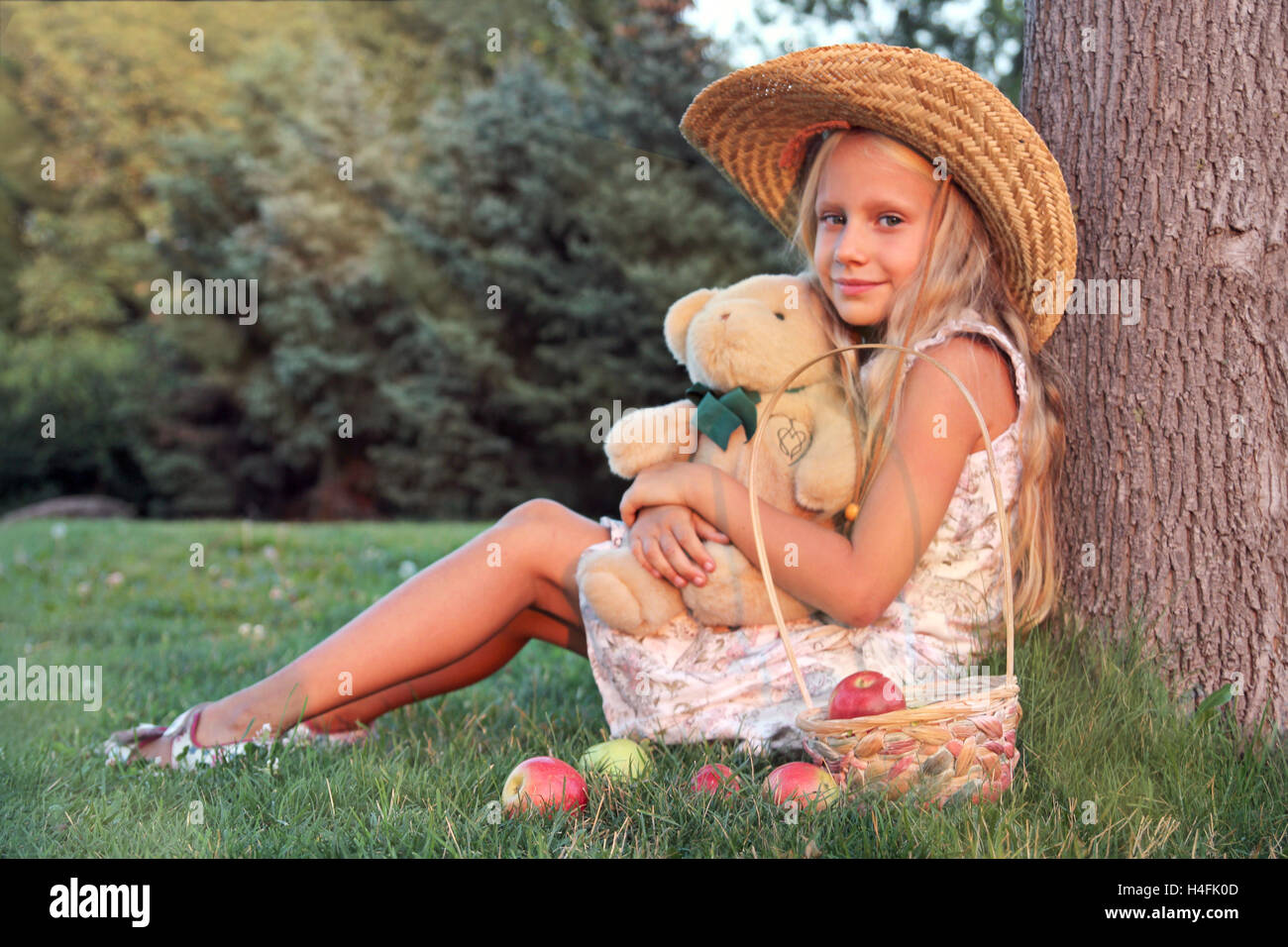Little girl with Teddy Bear and busket with apples sitting on grass ...