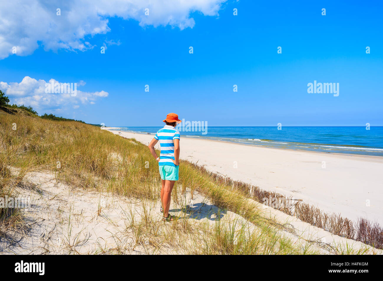 Young woman tourist standing on sand dune and looking at white sand beach in Bialogora, Baltic Sea, Poland Stock Photo
