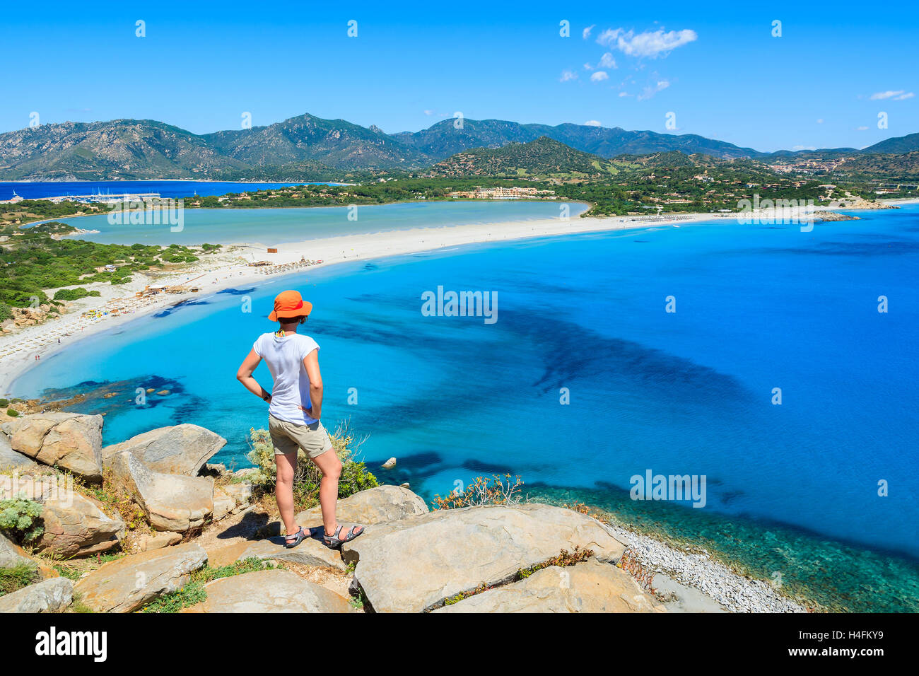 Young woman tourist standing on cliff looking at beautiful azure sea lagoon beach, Villasimius, Sardinia island, Italy Stock Photo