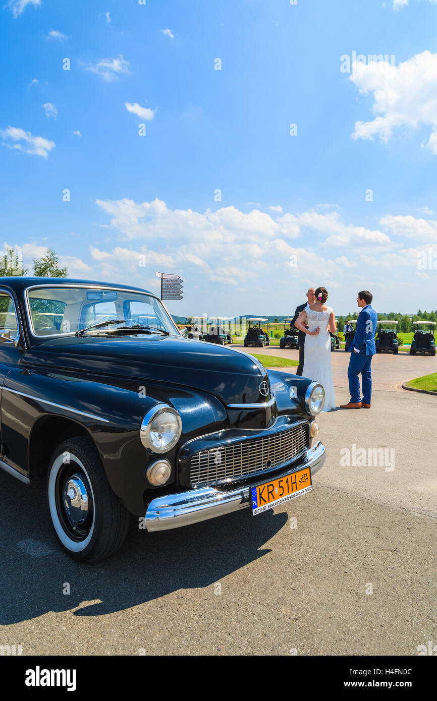 PACZULTOWICE GOLF CLUB, POLAND - AUG 9, 2014: old classic car parks on street in Paczultowice Golf Club with bride and groom couple in background just before weeding ceremony. Stock Photo