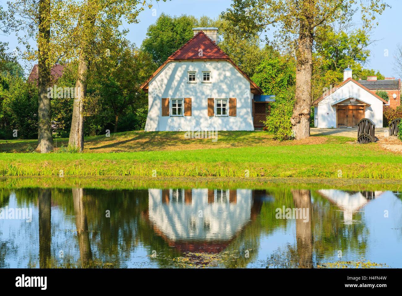 Reflection of traditional cottage house in water of lake near Radziejowice village, Poland Stock Photo