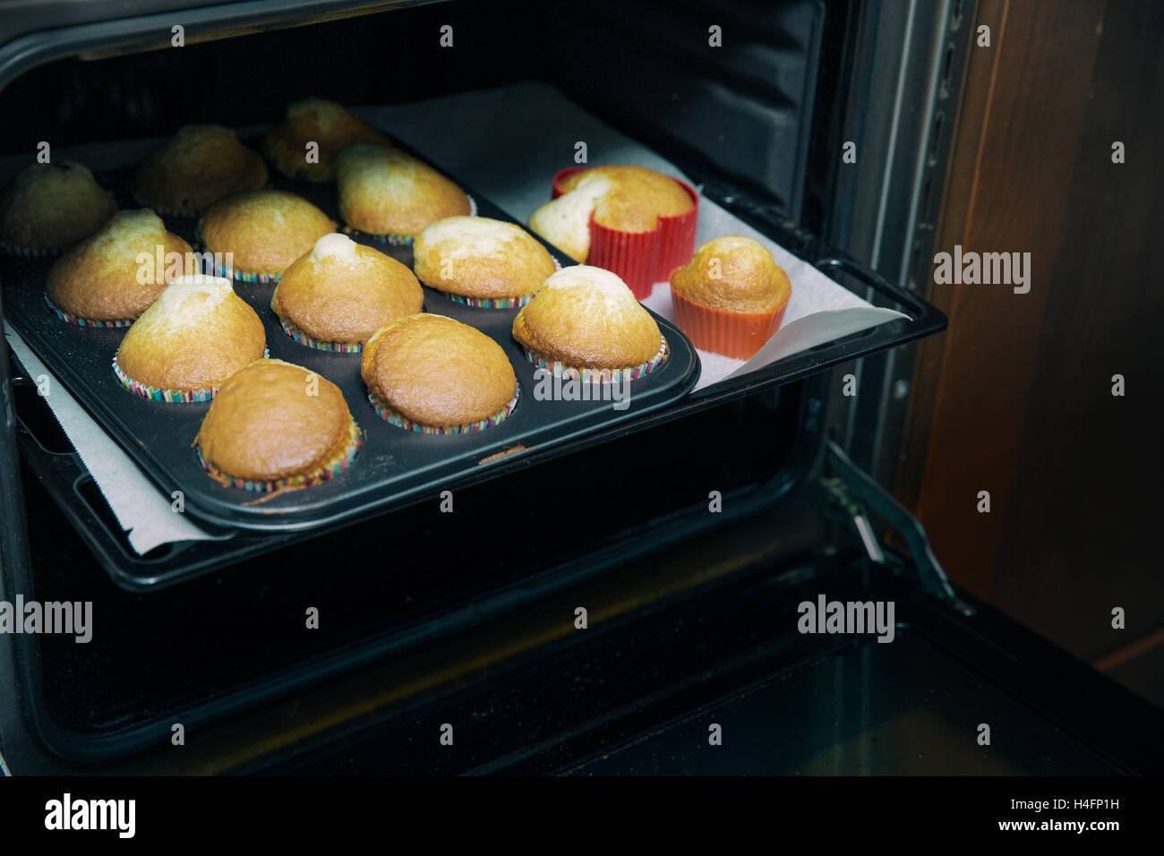 View of baked fresh cupcakes on tray in oven with open door Stock Photo