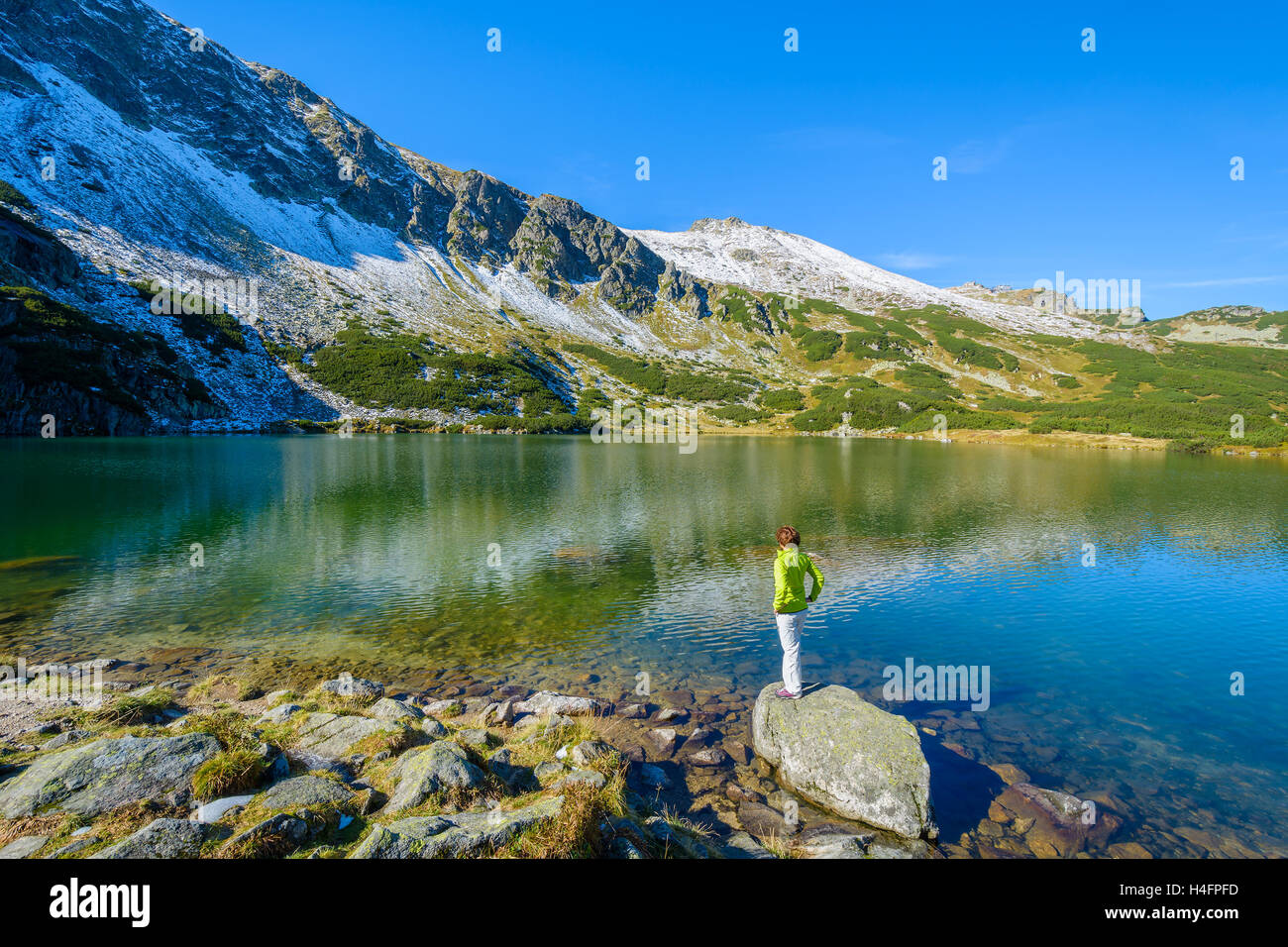 Young woman tourist looking at mountains and standing on a rock in alpine lake, Gasienicowa valley, High Tatra Mountains, Poland Stock Photo