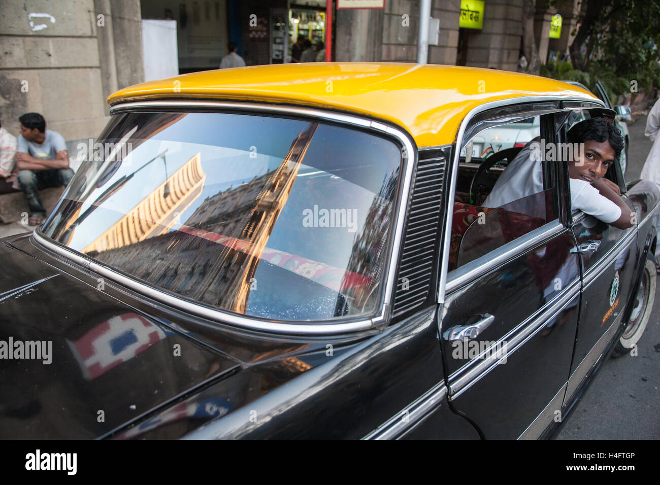 Traditional yellow and black Ambassador taxi in centre of Mumbai,Bombay with reflection of Indian Stock Exchange building.India. Stock Photo