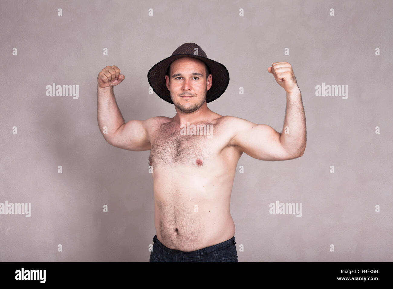 Shirtless man in hat posing and showing his strong arms and hairy body. Stock Photo