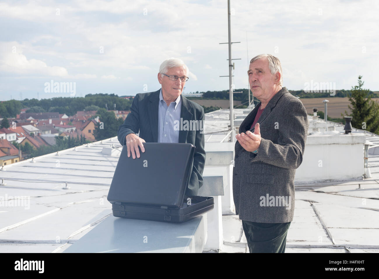Two senior businessmen with briefcase discussing business deal outdoors on the roof of a building. Stock Photo