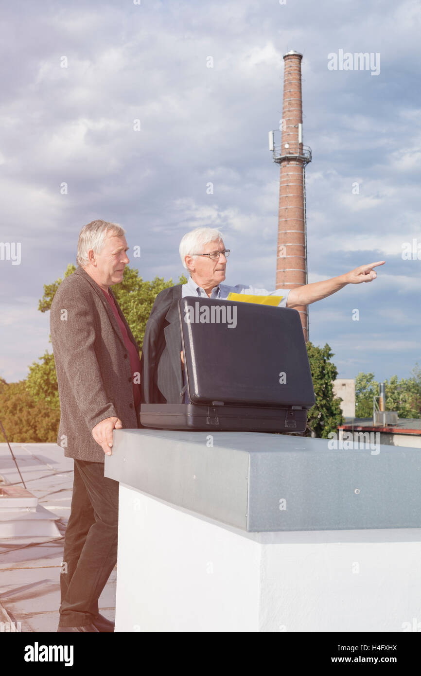Two senior businessmen with briefcase discussing business outdoors on the roof of a building. Stock Photo