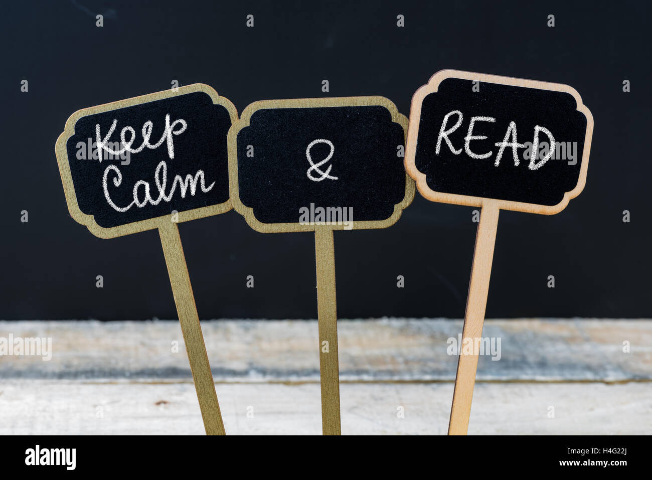 Keep Calm and Read message written with chalk on mini blackboard labels, defocused chalkboard and wooden table in background. Stock Photo