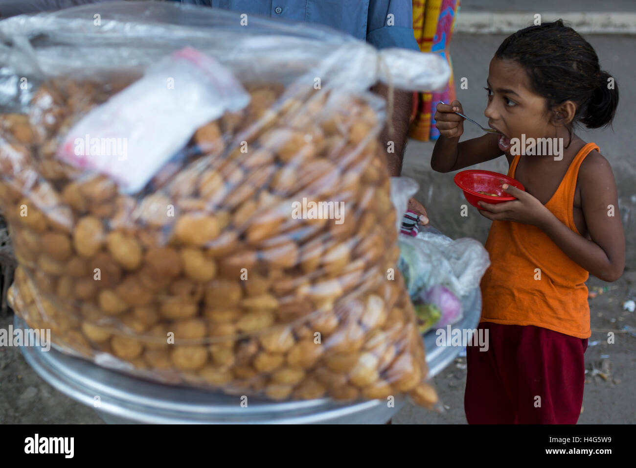 DHAKA, BANGLADESH - OCTOBER 15 : A child eating street food in Dhaka, Bangladesh, on October 15, 2016. Most of time food are being prepared with unhygienic handling. And those food are being sold in open air in a dirty city, which carry many germs. Unhygienic food items that are being sold on the streets of the capital are exposing the consumers to serious health hazards. Thousands of people are taking these foods everyday attracted by their cheap price and fine taste, not knowing what a great danger they are inviting for themselves by eating them.  Some 600 million people fall ill each year f Stock Photo