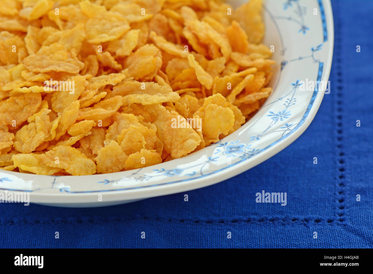 Crisp golden organic corn flakes in pretty blue and white bowl on vibrant blue napkin in horizontal format.  Macro with shallow Stock Photo