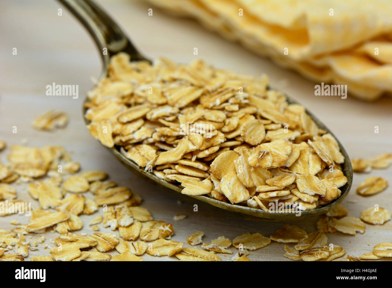 Old fashioned whole grain rolled oats with vintage silver spoon on rustic wood with yellow napkin in background.  Shallow depth Stock Photo
