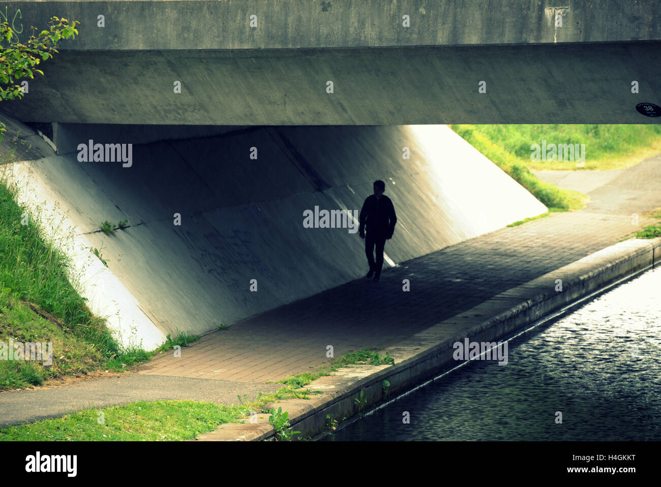 Ominous s threatening silhouette of boy passing through tunnel beside canal Stock Photo