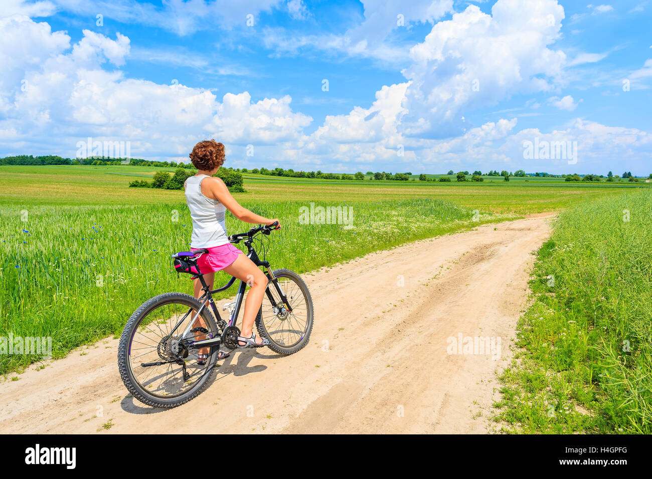 Young attractive woman riding a bike on rural road in green summer landscape, Poland Stock Photo