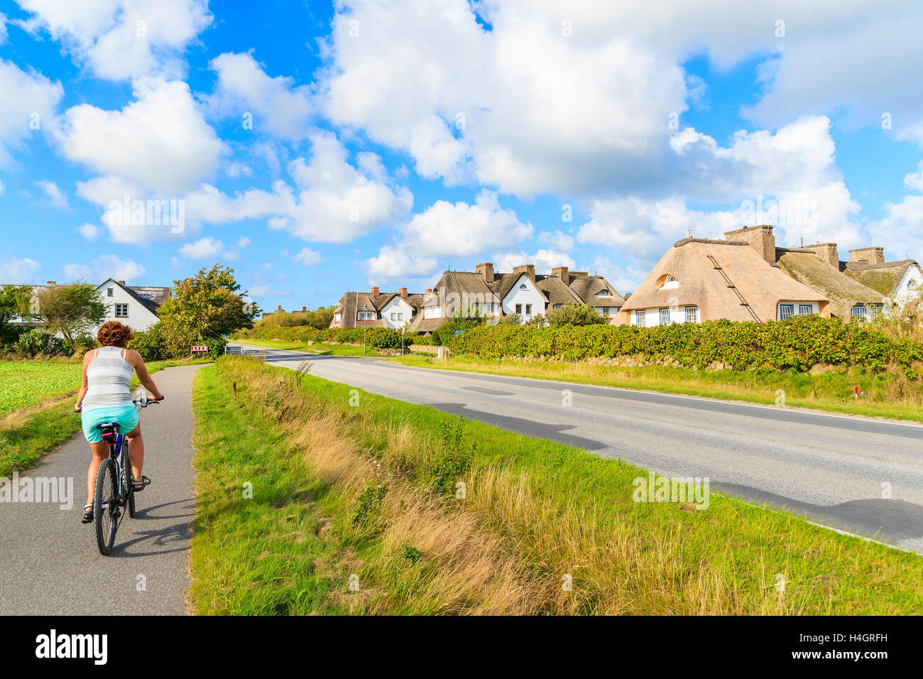 Young woman tourist rinding a bike along a road in Keitum village with typical straw roof houses on Sylt island, Germany Stock Photo