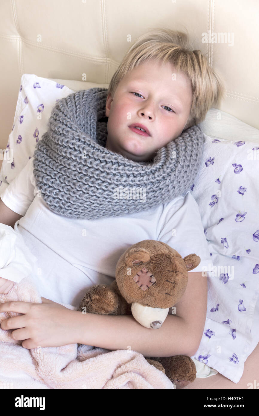 Sick child (blond boy, kid) lying in bed with teddy bear Stock Photo