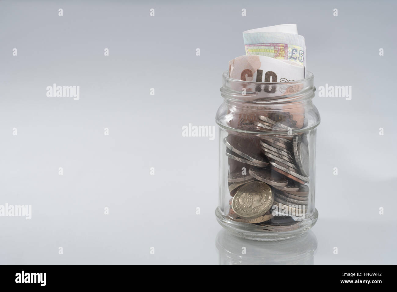 Picture of jam jar with loose change & money. Metaphor cost of living, disposable income, rainy day savings/saving money concept, saving pot, poverty. Stock Photo
