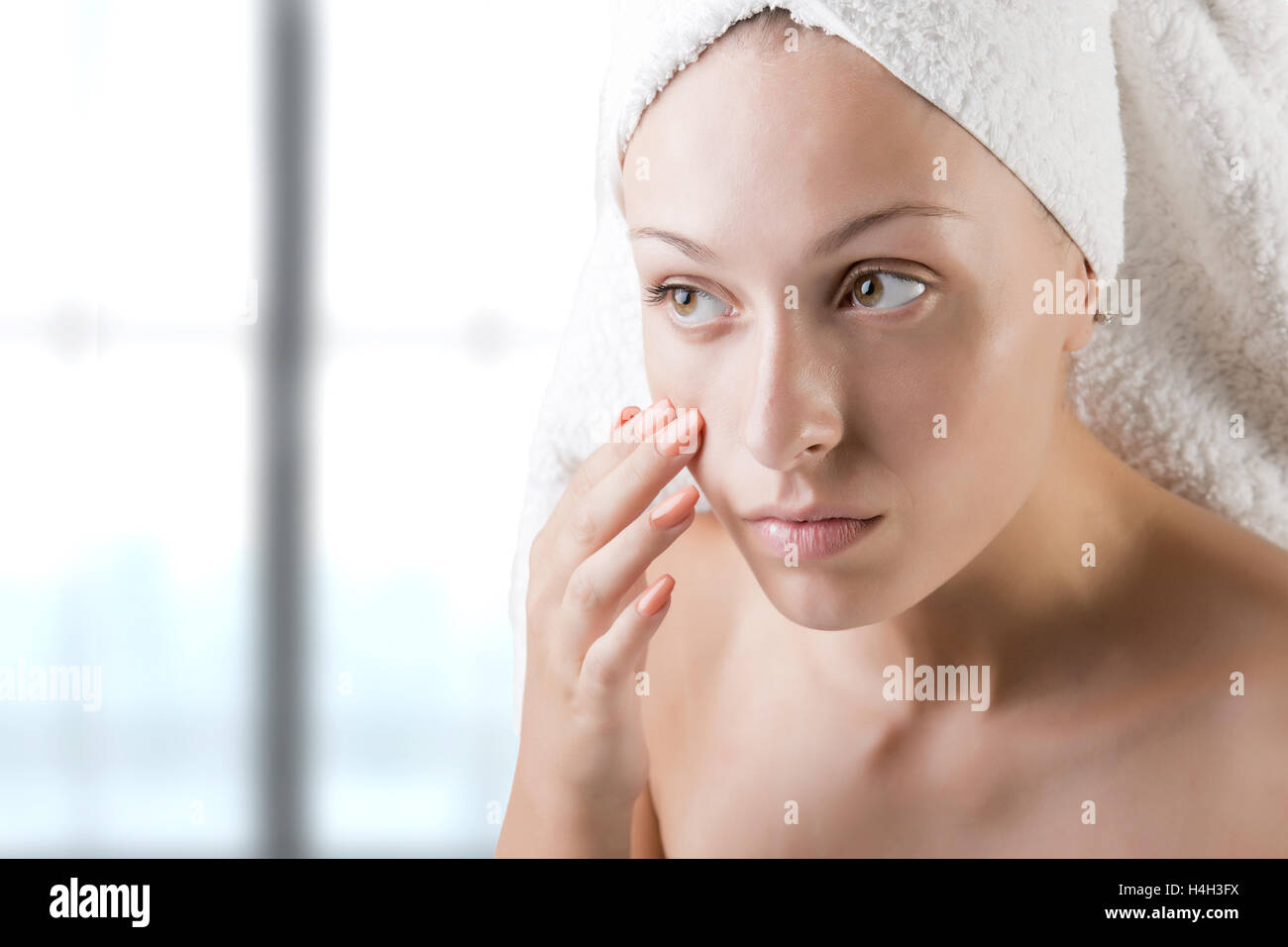 Woman with a towel wrapped around her head checking her skin Stock Photo