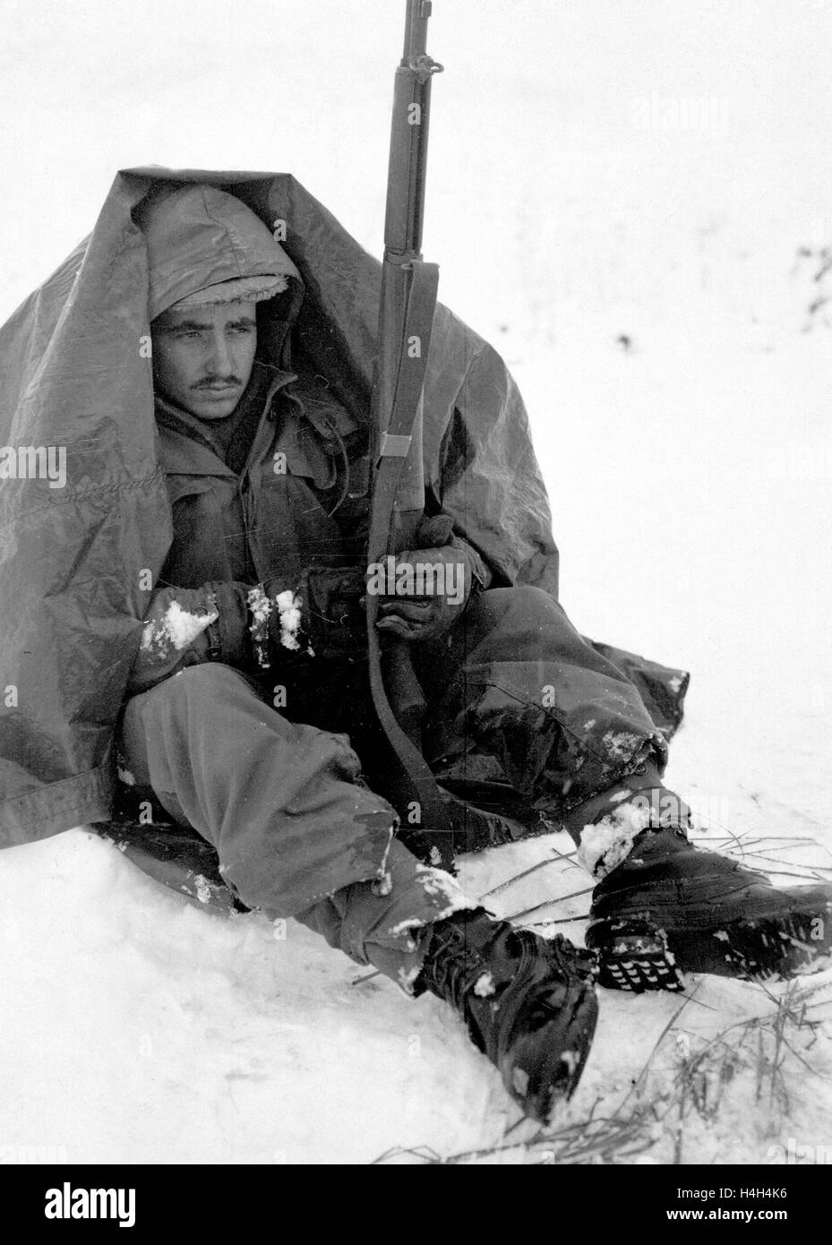 U.S. soldier Pfc. Preston McKnight, with the 19th Infantry Regiment, uses his poncho to get protection from the biting wind and cold during the Korean War January 10, 1951 in Yoju, Korea. Stock Photo