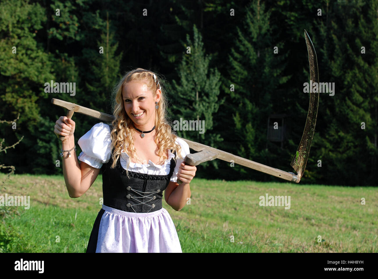 Farm girl with a scythe, wearing a dirndl, a traditional German or Austrian dress Stock Photo