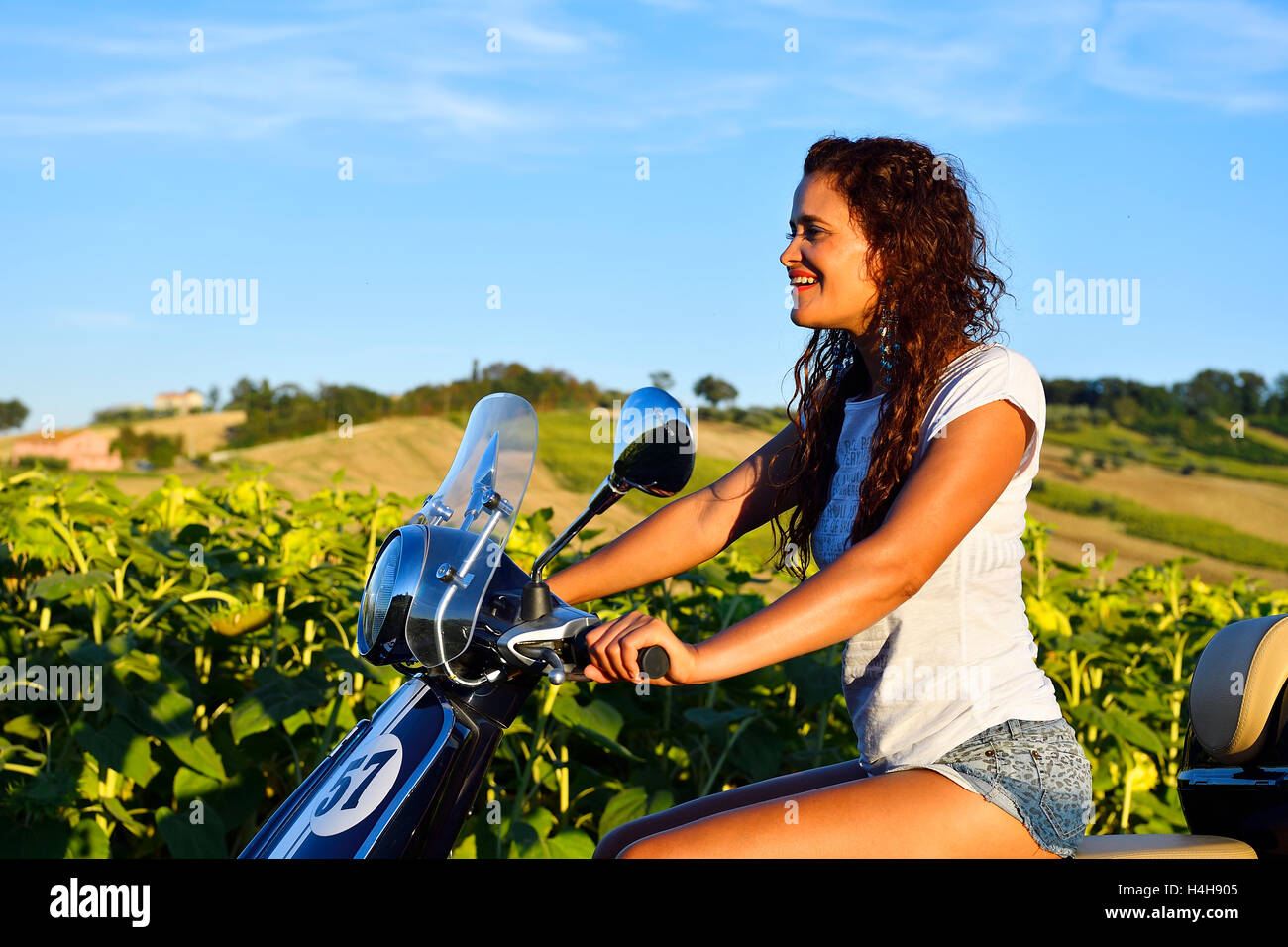 Woman on Vespa Primavera scooter in front of sunflower field, Sant&#39;Amico, Morro d&#39;Alba, Marche, Italy Stock Photo