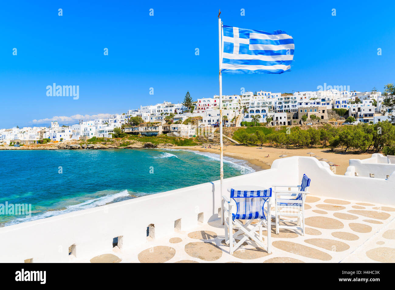 Greek flag waving on a terrace overlooking Piperi beach in Naossa village, Paros island, Cyclades, Greece Stock Photo