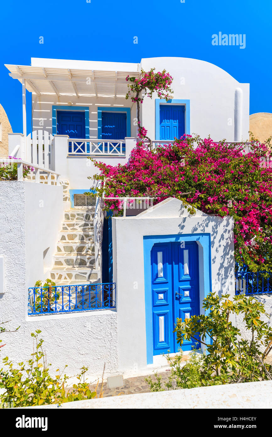 Typical white and blue Greek house decorated with red flowers in Oia village on Santorini island, Greece Stock Photo