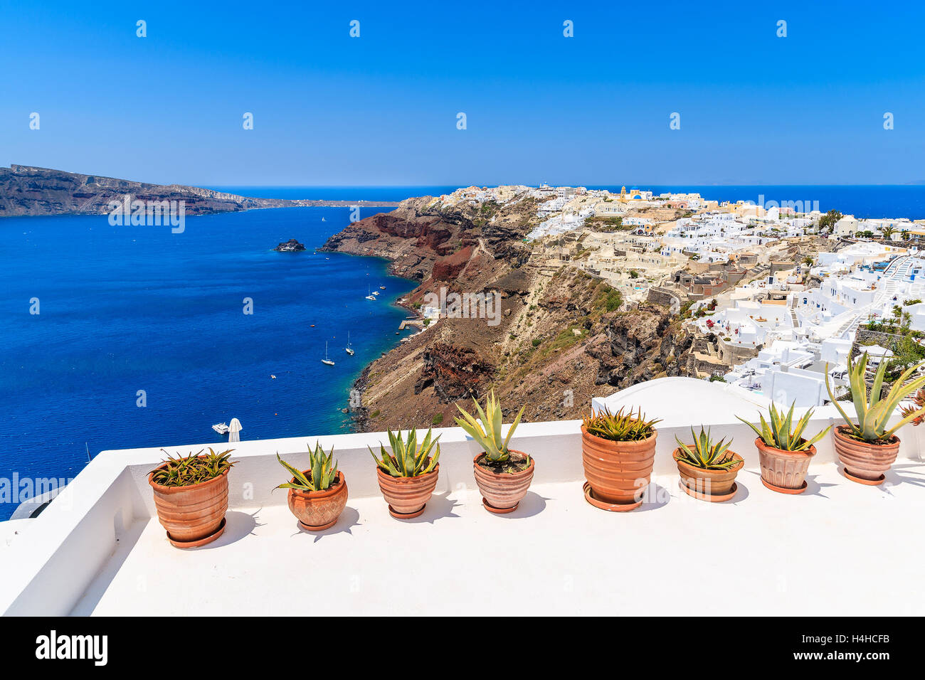 Plants in pots on terrace with view of Oia village on top of volcano cliff, Santorini island, Greece Stock Photo